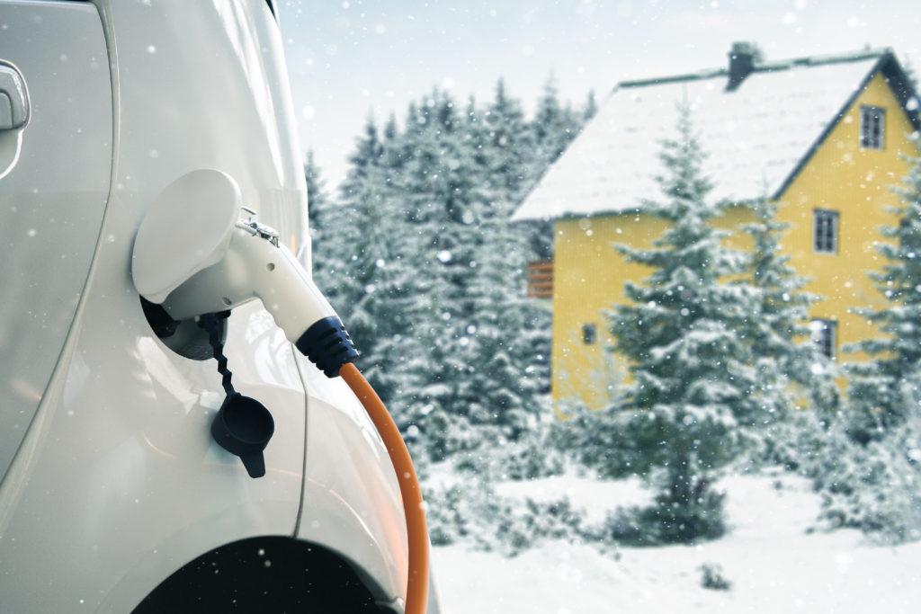 Elektroauto vor Winterlandschaft und schneebedeckten Bäumen