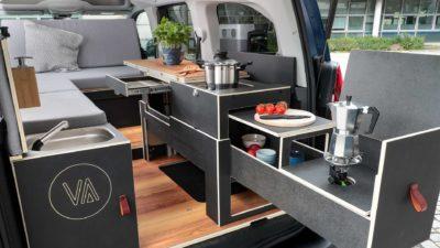 Innenraum des Camper-Vans Peugeot E-Rifter Vanderer mit ausgezogener Küche, Kochfeld, Kaffeekocher und Sitzgelegenheiten