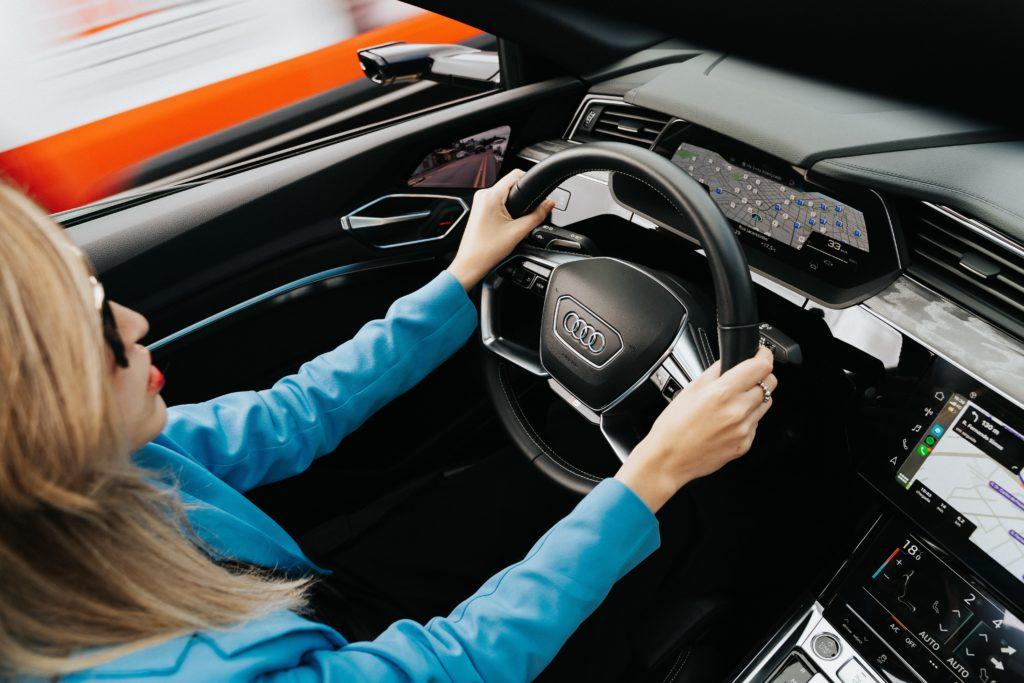 Blonde Autofahrerin mit beiden Händen am Lenkrad eines Audis von schräg oben fotografiert